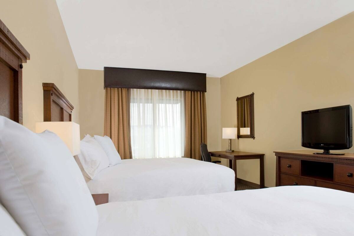 A hotel room with two beds, a desk, a television, and a window with curtains.