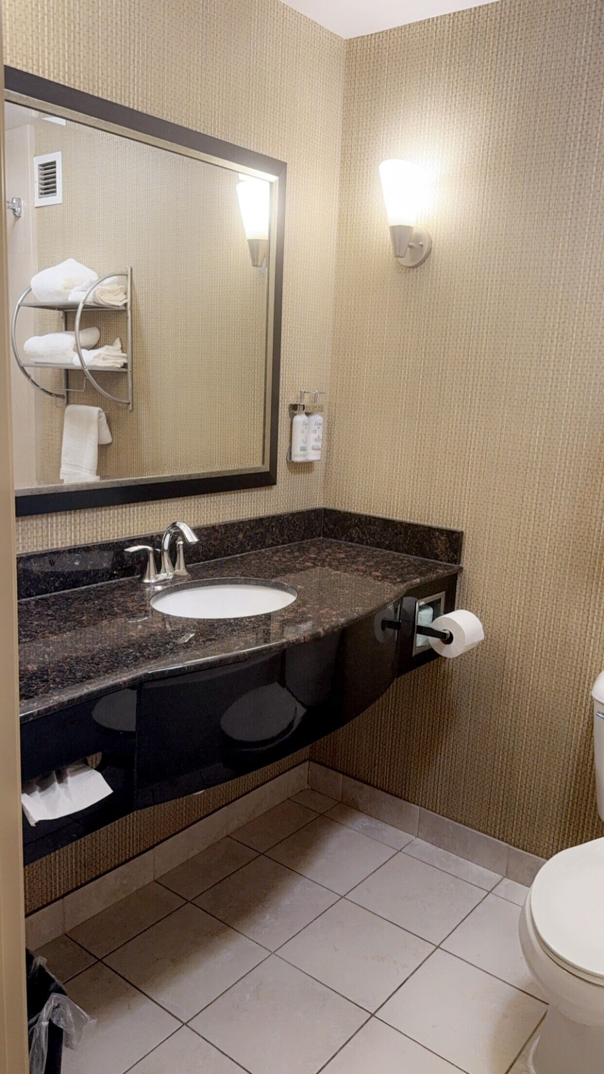 A bathroom with a sink, mirror, towel rack, toilet, and a trash bin.
