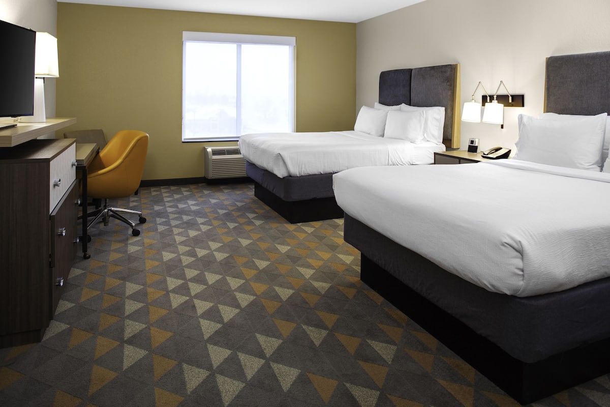 A hotel room with two beds, a desk with a lamp, a chair, and a large window.