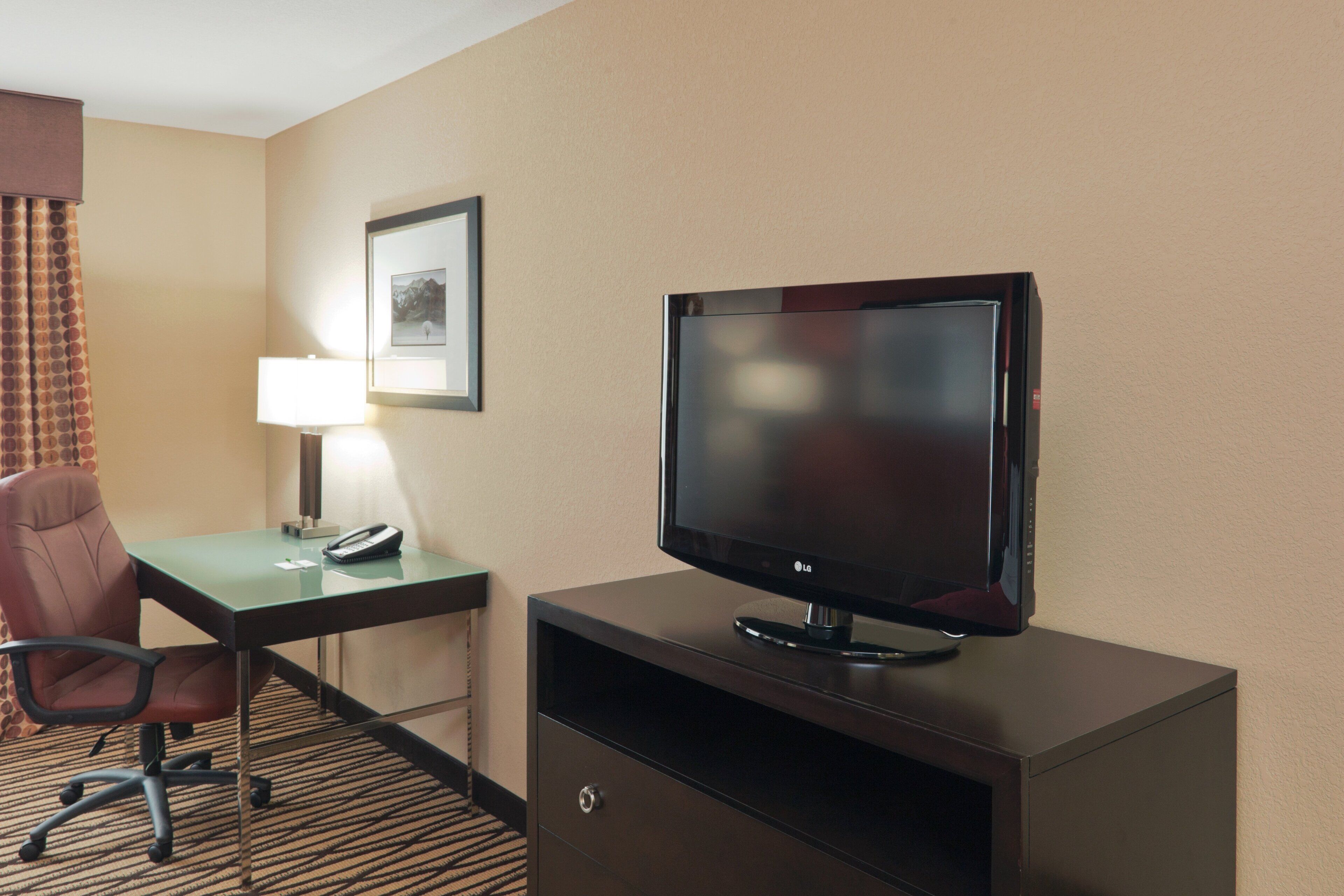 A hotel room with a desk, chair, television, and a framed picture on the wall.