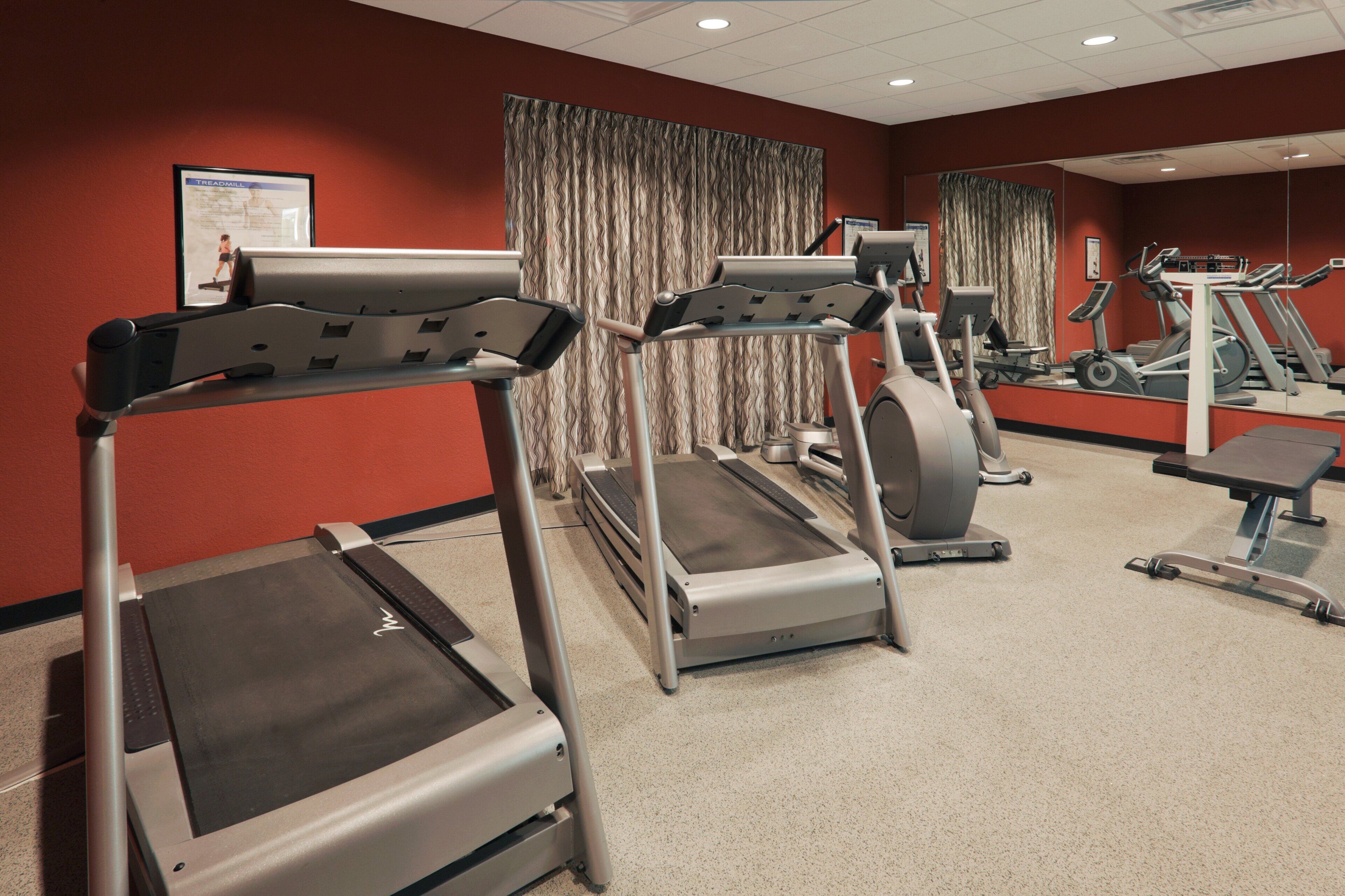 A gym with treadmills, stationary bikes, and a mirrored wall.
