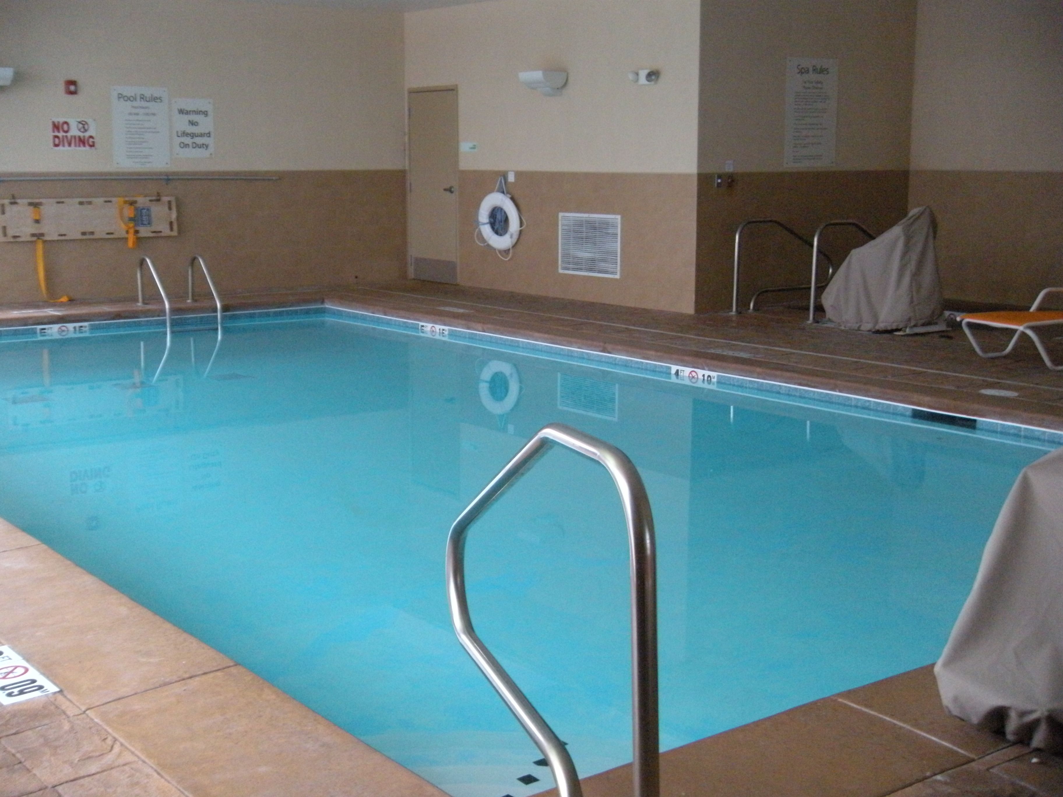 An indoor swimming pool with clear water, a lifeguard chair, and a pool rule sign on the wall.