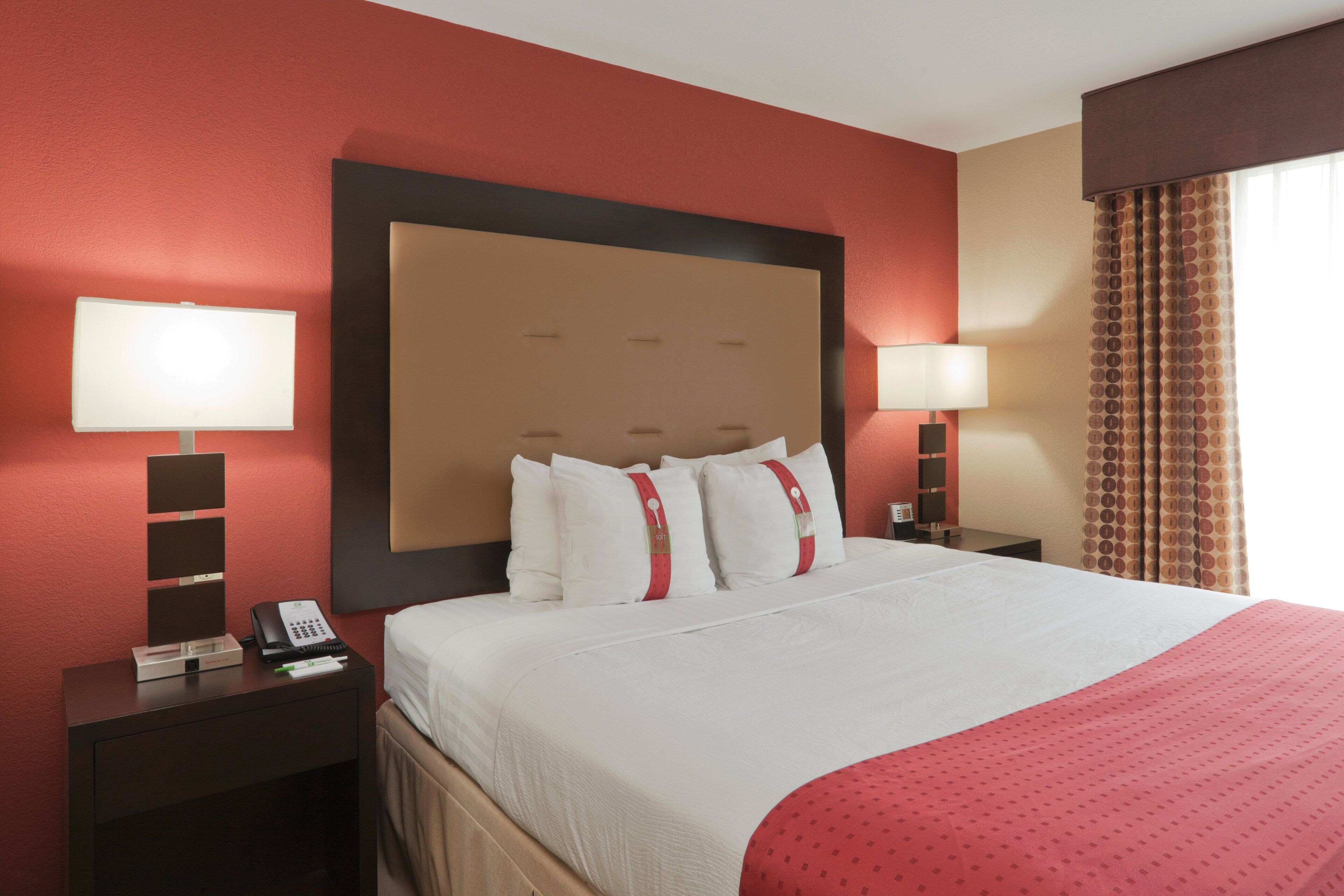 A hotel room with a large bed, two bedside tables, a telephone, and a lamp on each side.