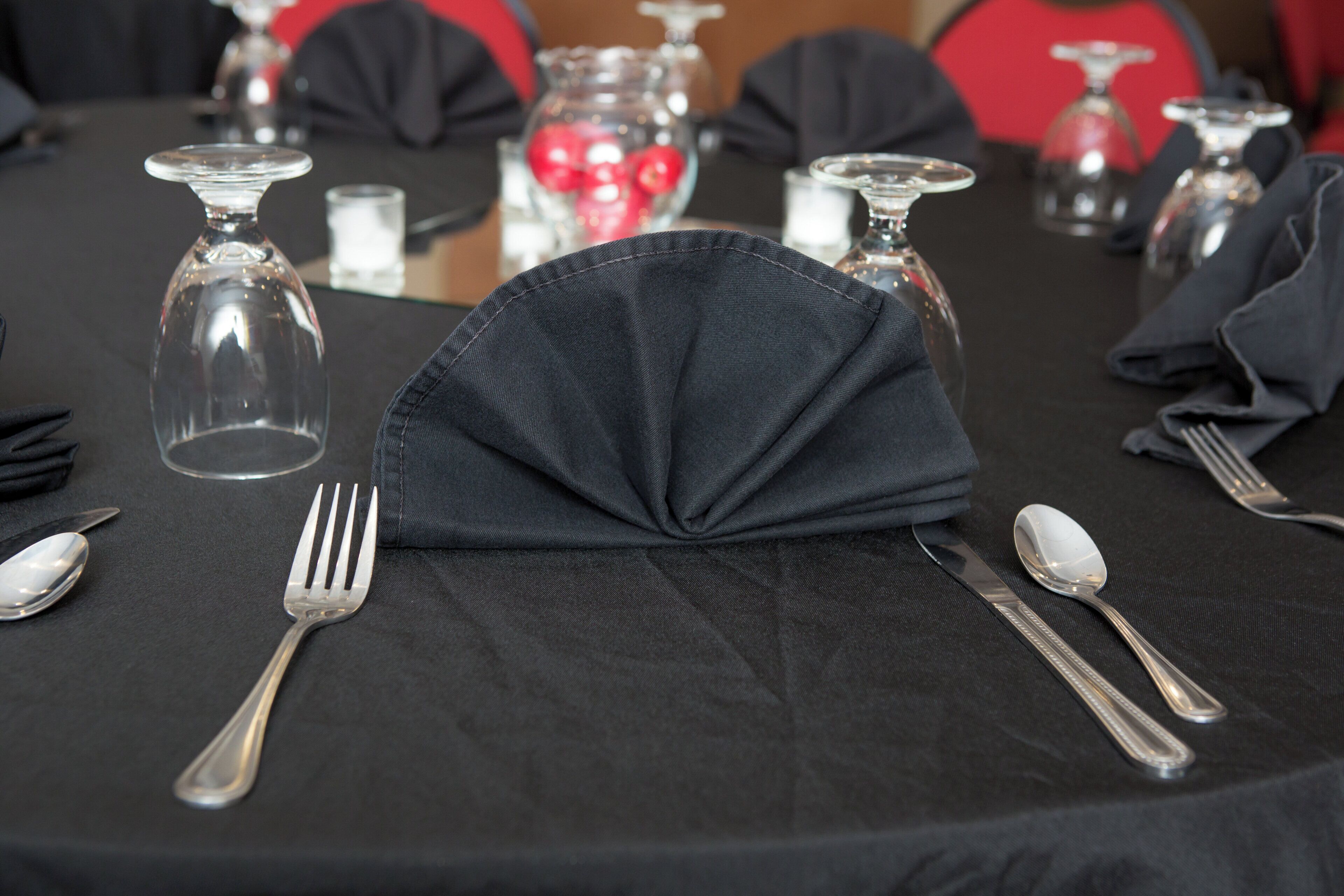 Une table dressée avec une nappe noire, des couverts en argent et de la verrerie transparente.