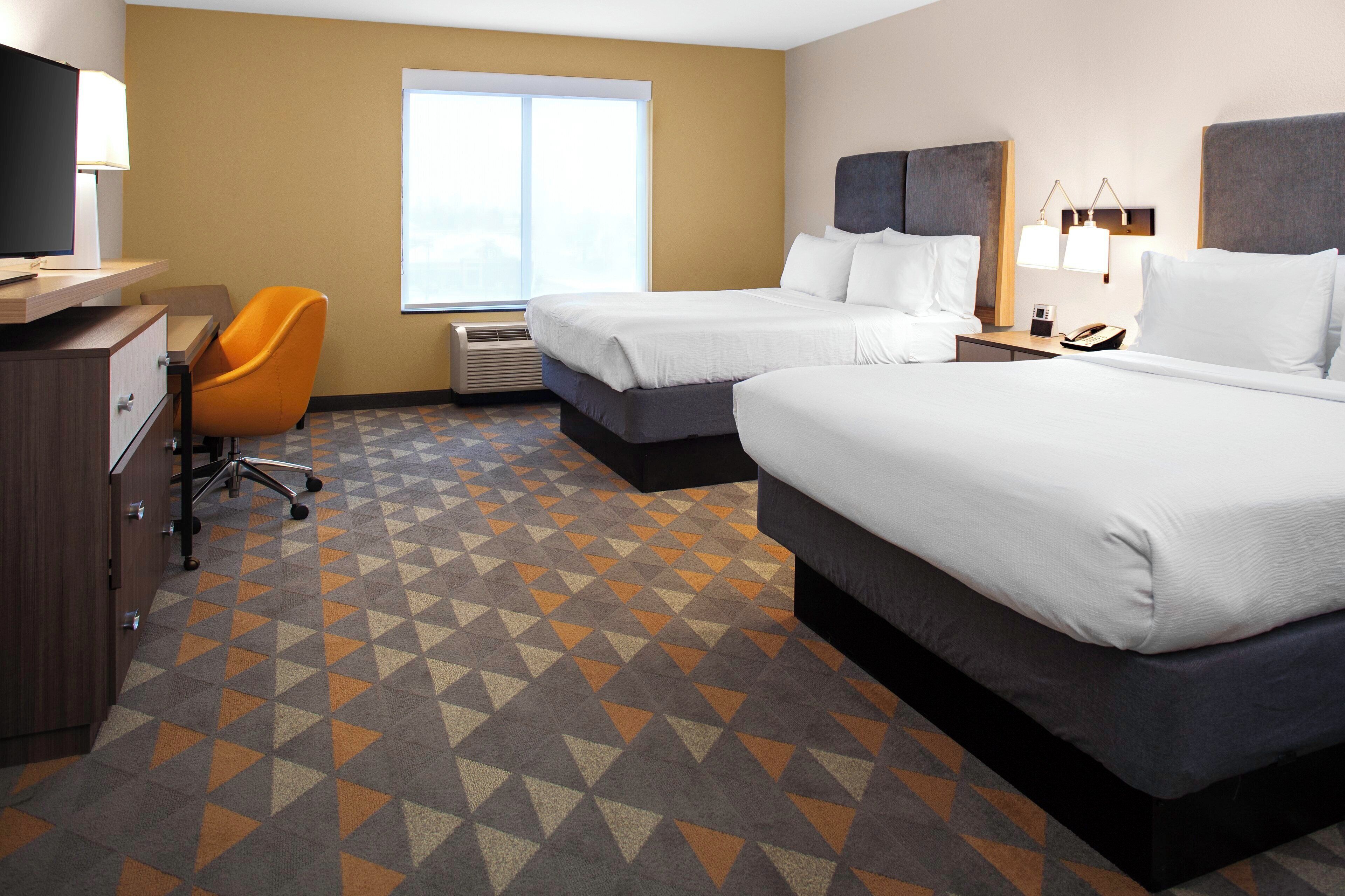 A hotel room with two beds, a desk, a chair, and a large window.