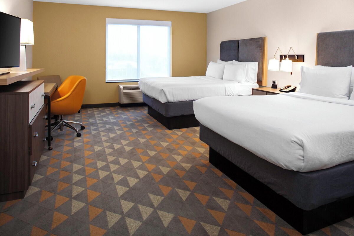 A hotel room with two beds, a desk, a chair, and a large window.