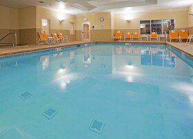 Una amplia piscina interior con agua cristalina, rodeada de sillones reclinables color naranja y un reloj en la pared.