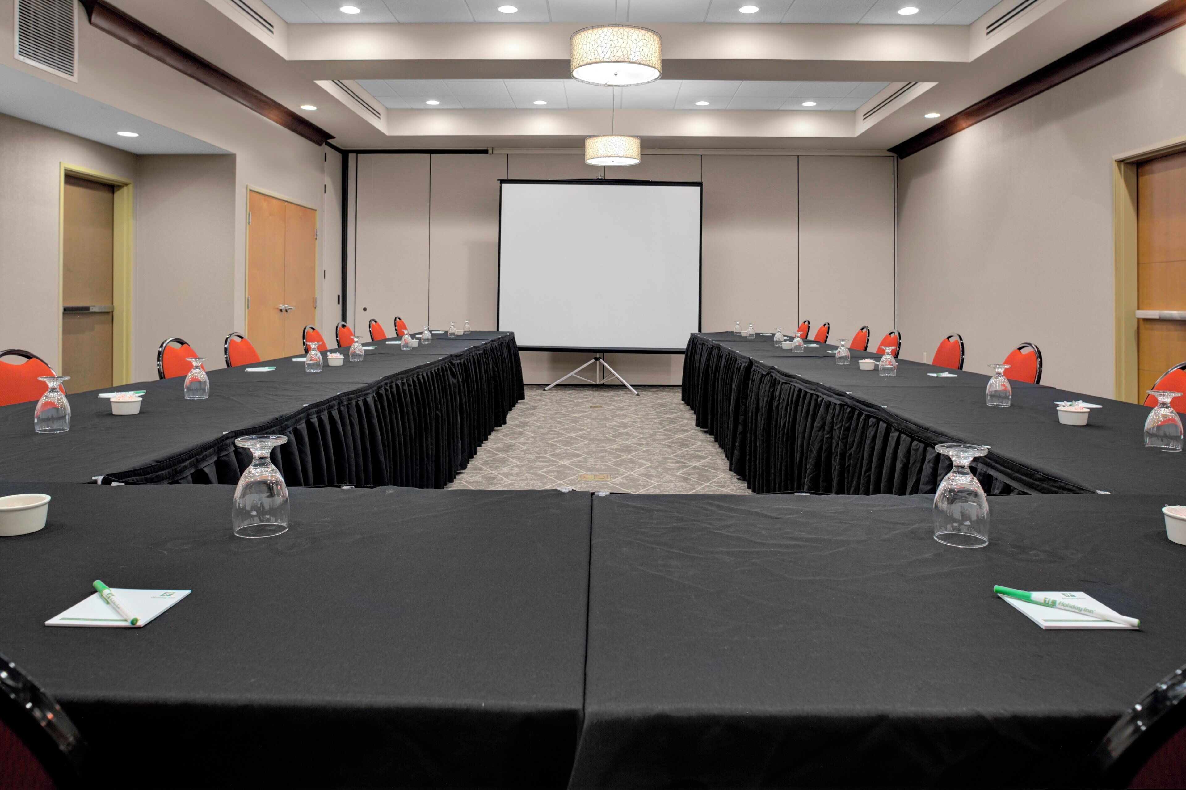 A conference room with a long table, chairs, a projector screen, and a podium.