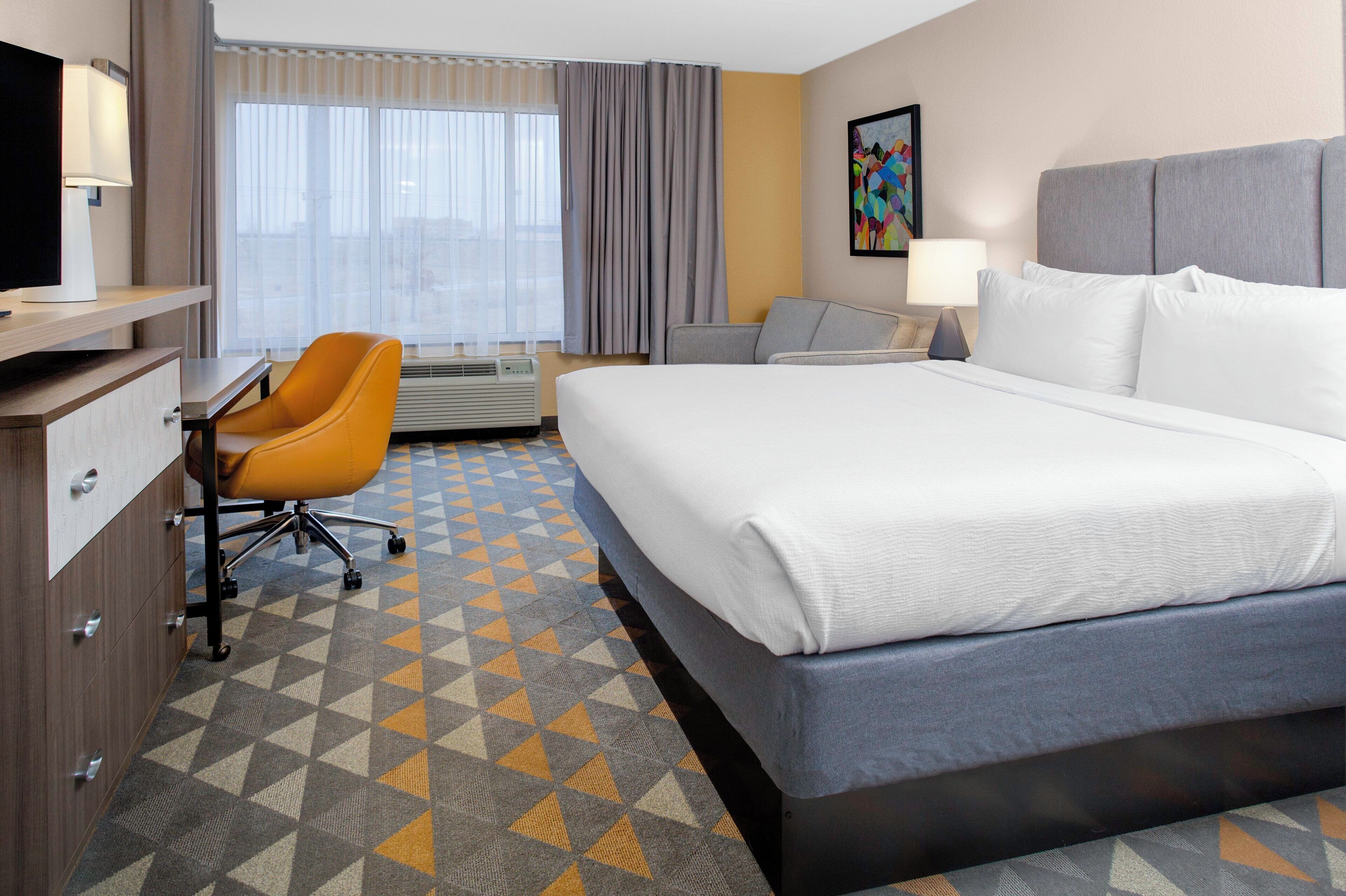 A hotel room with a bed, a desk, a chair, and a window with curtains.