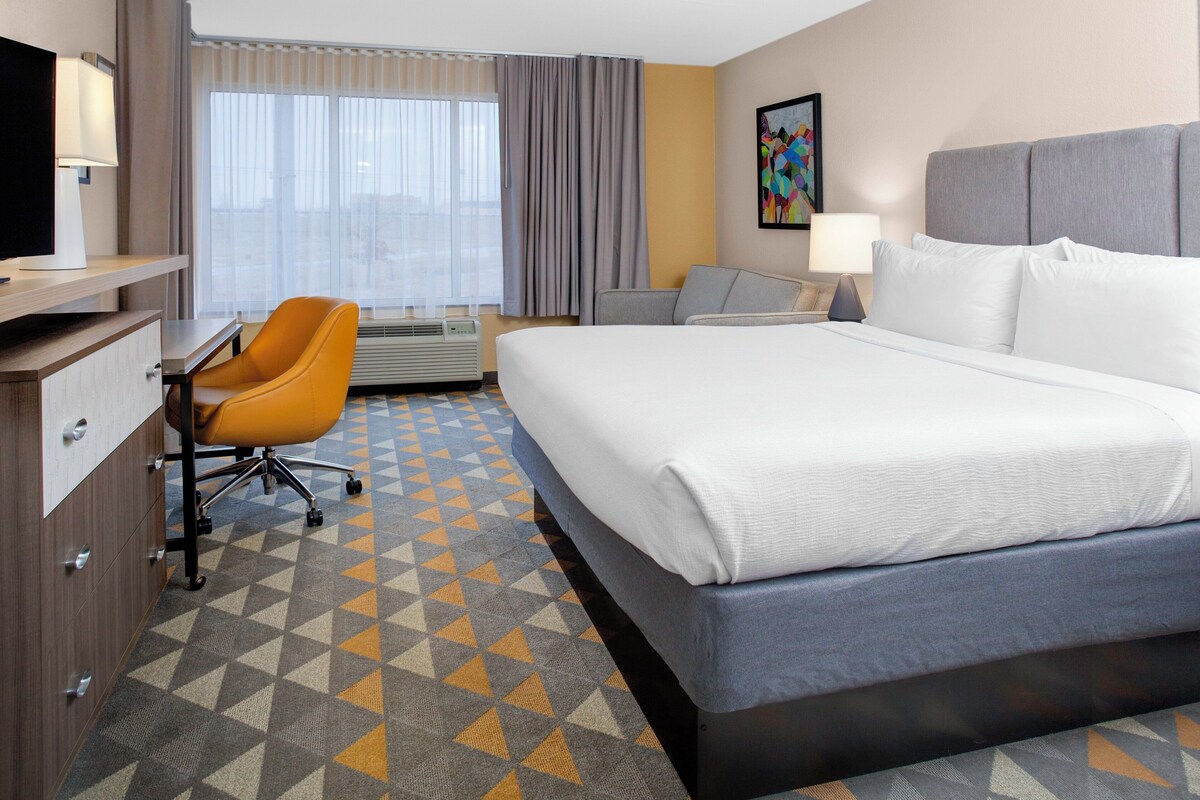 A hotel room with a bed, a desk, a chair, and a window with curtains.