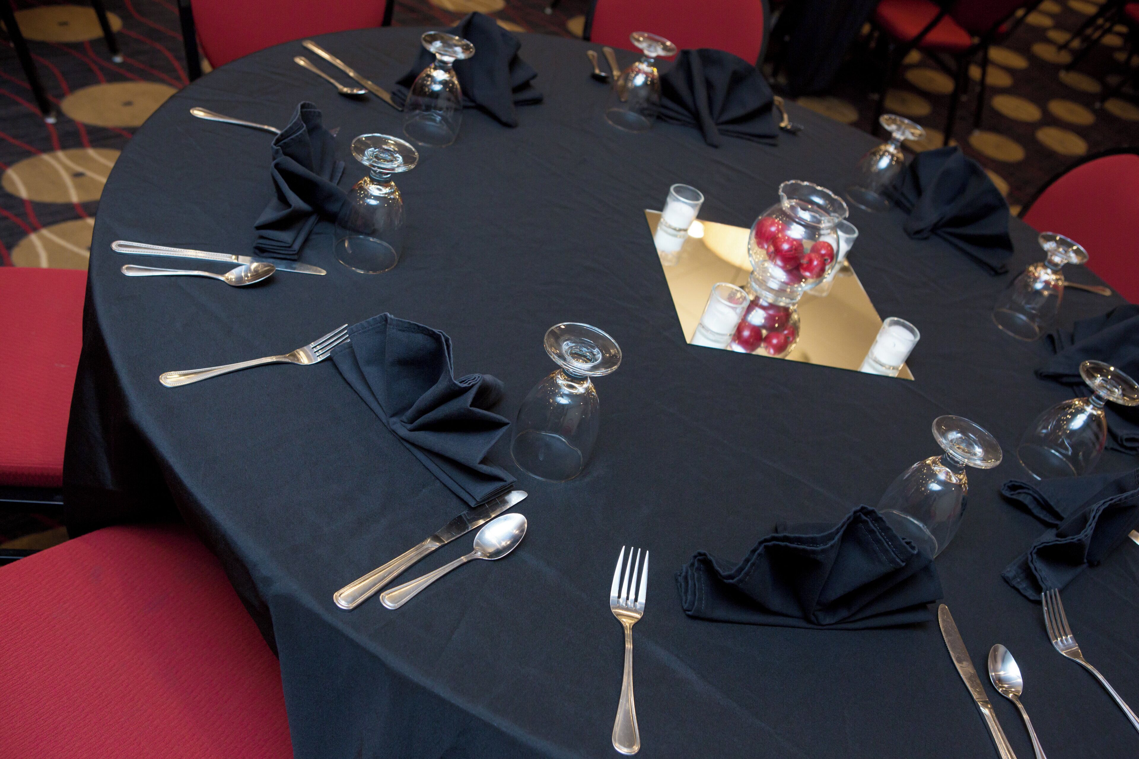 Mesa redonda lista para una comida, con cubiertos, copas y un centro de mesa.