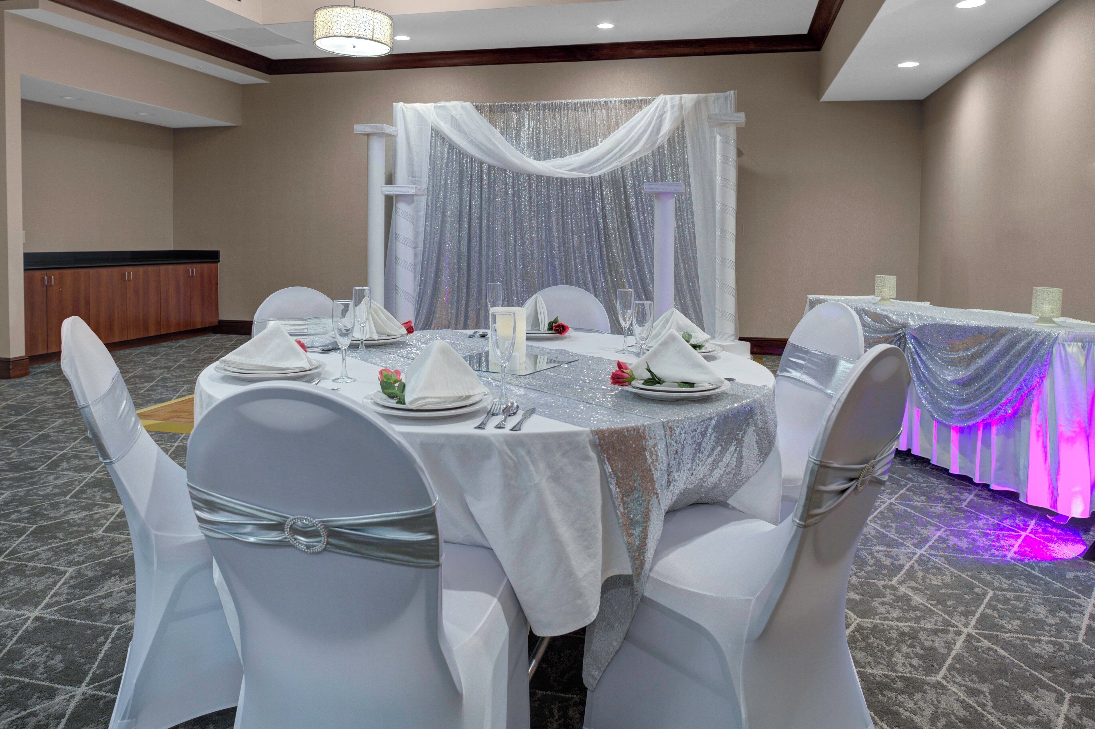 Un salón de banquetes con mesas redondas dispuestas para un evento formal, con manteles blancos, cubiertos y cristalería.