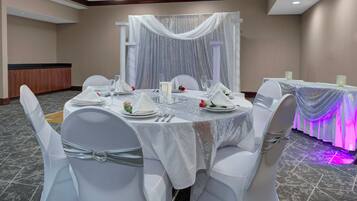 Un salón de banquetes con mesas redondas dispuestas para un evento formal, con manteles blancos, cubiertos y cristalería.