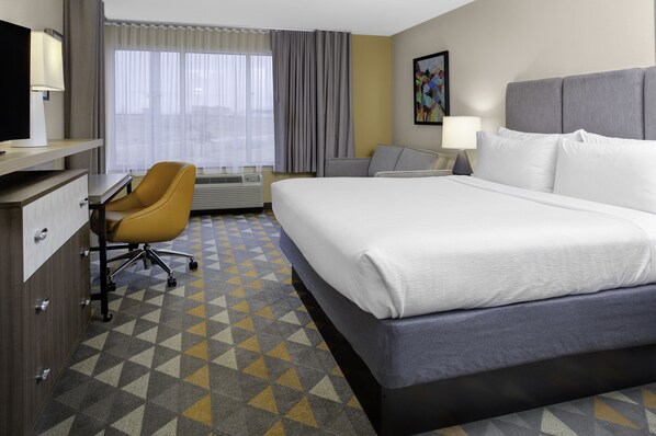 Habitación de hotel con una cama grande, un escritorio con silla, una ventana con cortinas y un cuadro en la pared.