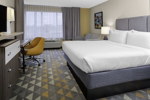 Habitación de hotel con una cama grande, un escritorio con silla, una ventana con cortinas y un cuadro en la pared.