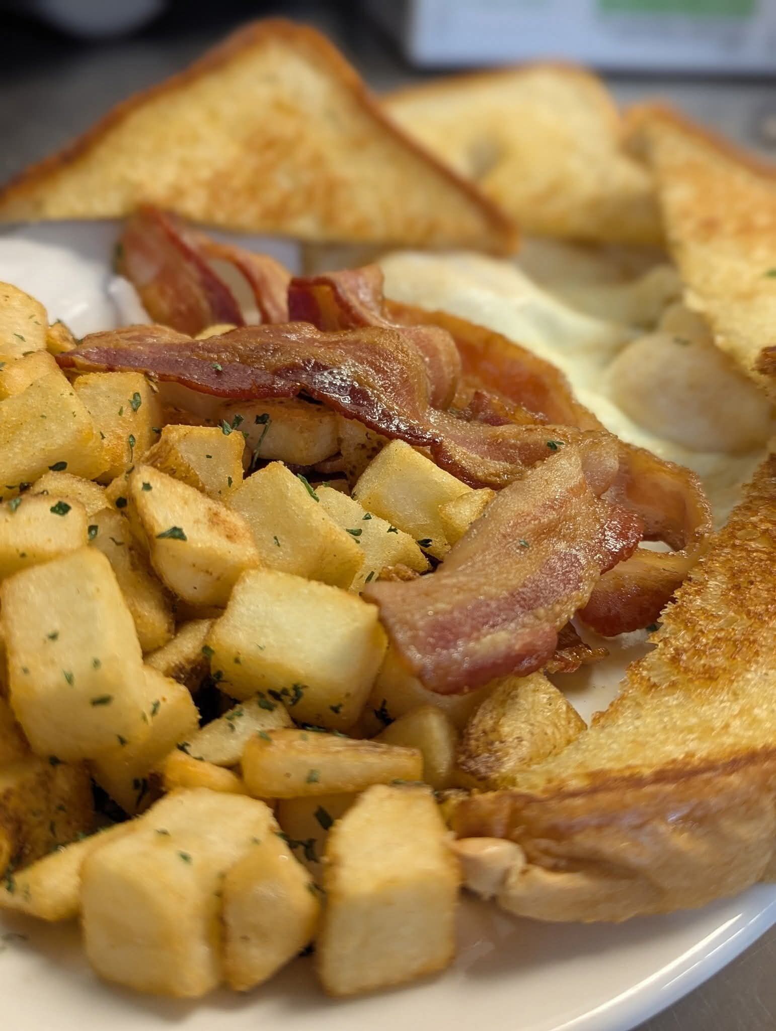 Une assiette de nourriture comprenant des toasts, des pommes de terre et du bacon.