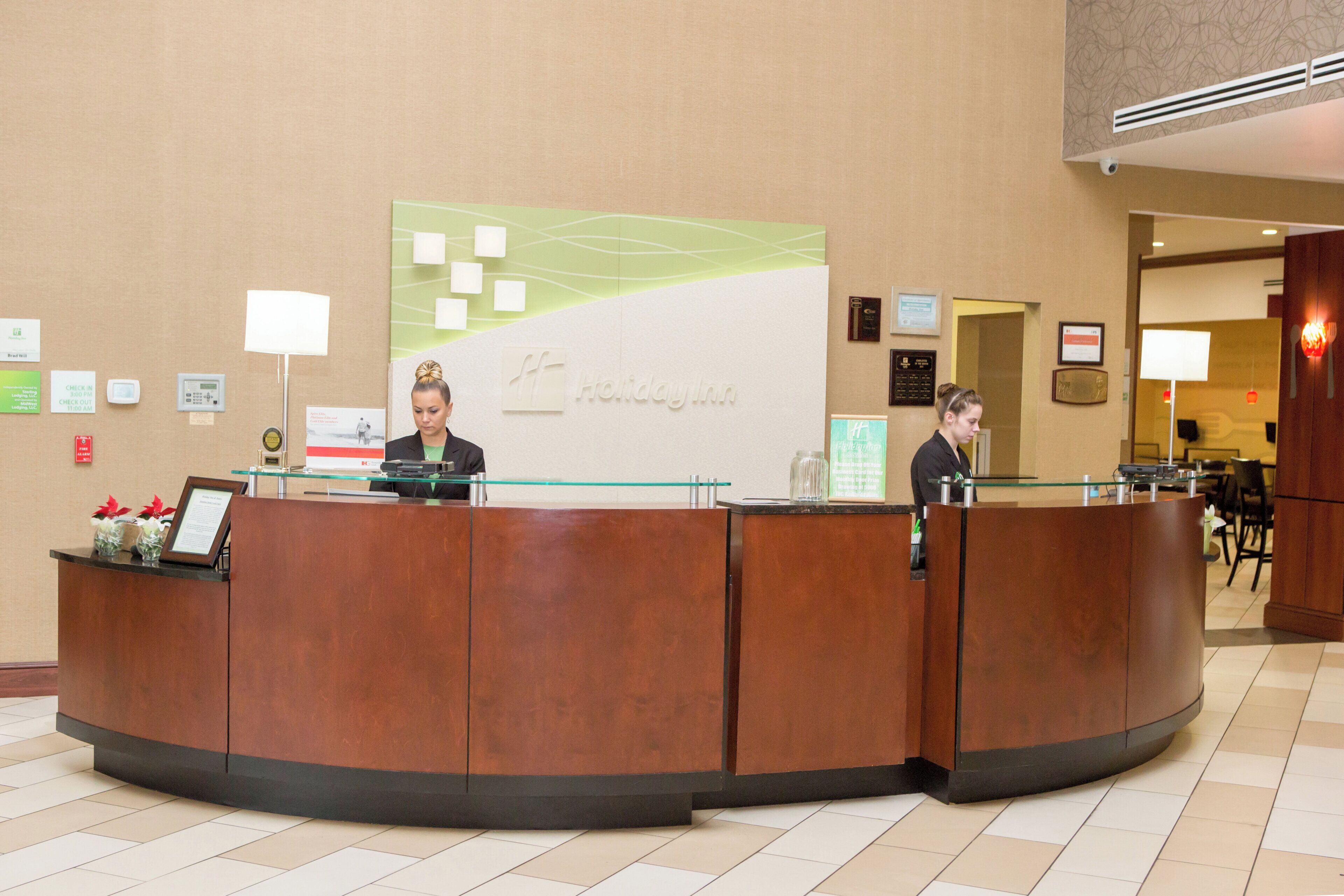 A reception desk with a Holiday Inn sign, a check-in counter, and a wall with various informational posters.