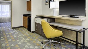 A hotel room with a desk, a yellow chair, a television, a kitchen area, and a patterned floor. - Holiday Inn Hotel & Suites Lima by IHG (Lima)