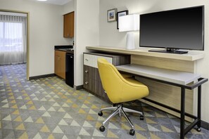A hotel room with a desk, a yellow chair, a television, a kitchen area, and a patterned floor. - Holiday Inn Hotel & Suites Lima by IHG (Lima)