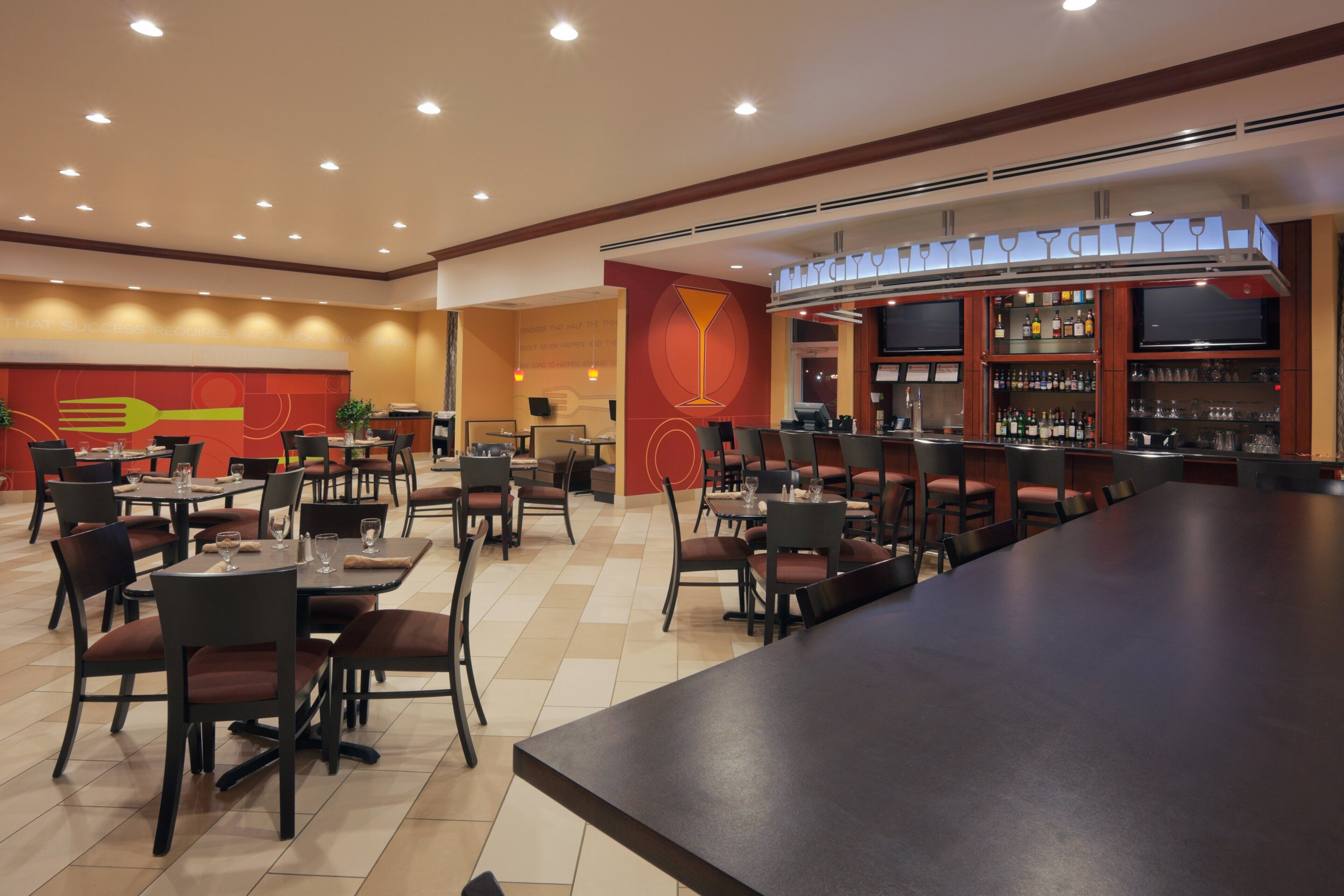 A restaurant with multiple tables and chairs, a bar area, and a large wall with a prominent design.