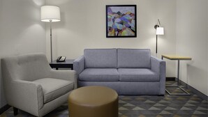 A room with a grey sofa, a grey armchair, a round ottoman, a small table with a lamp, and a framed abstract painting on the wall. - Holiday Inn Hotel & Suites Lima by IHG (Lima)
