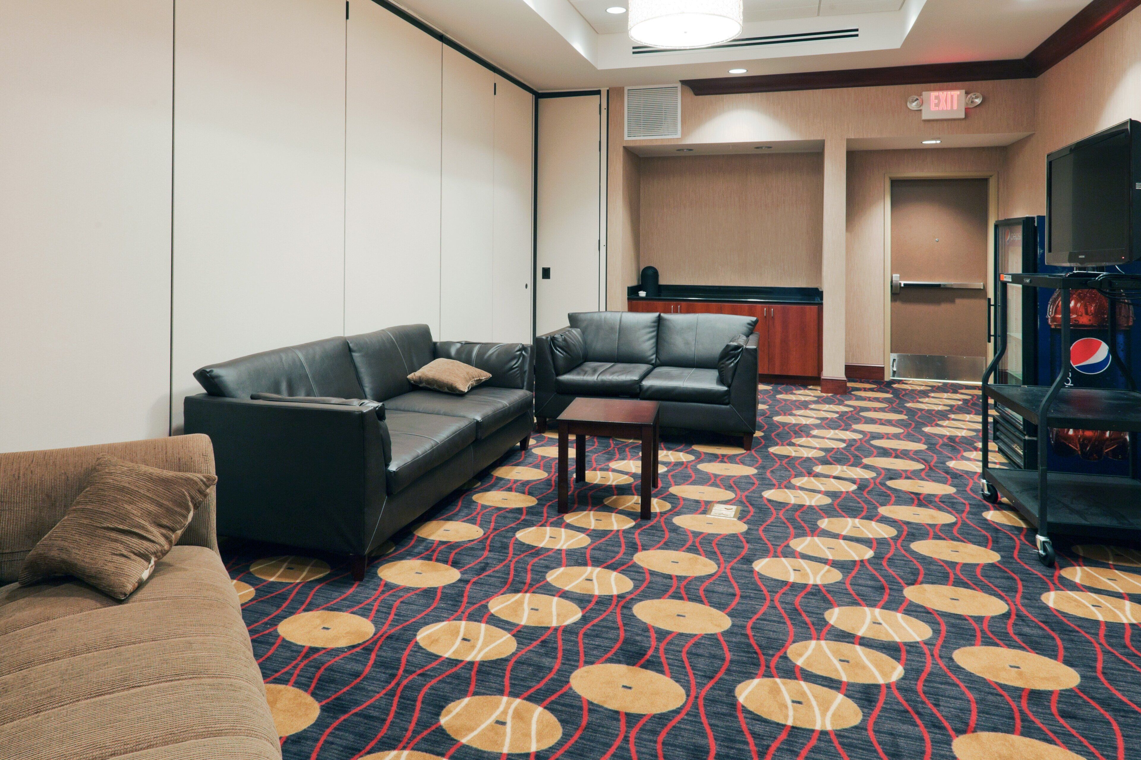 Une chambre d’hôtel avec deux canapés en cuir, une petite table et une moquette à motifs.