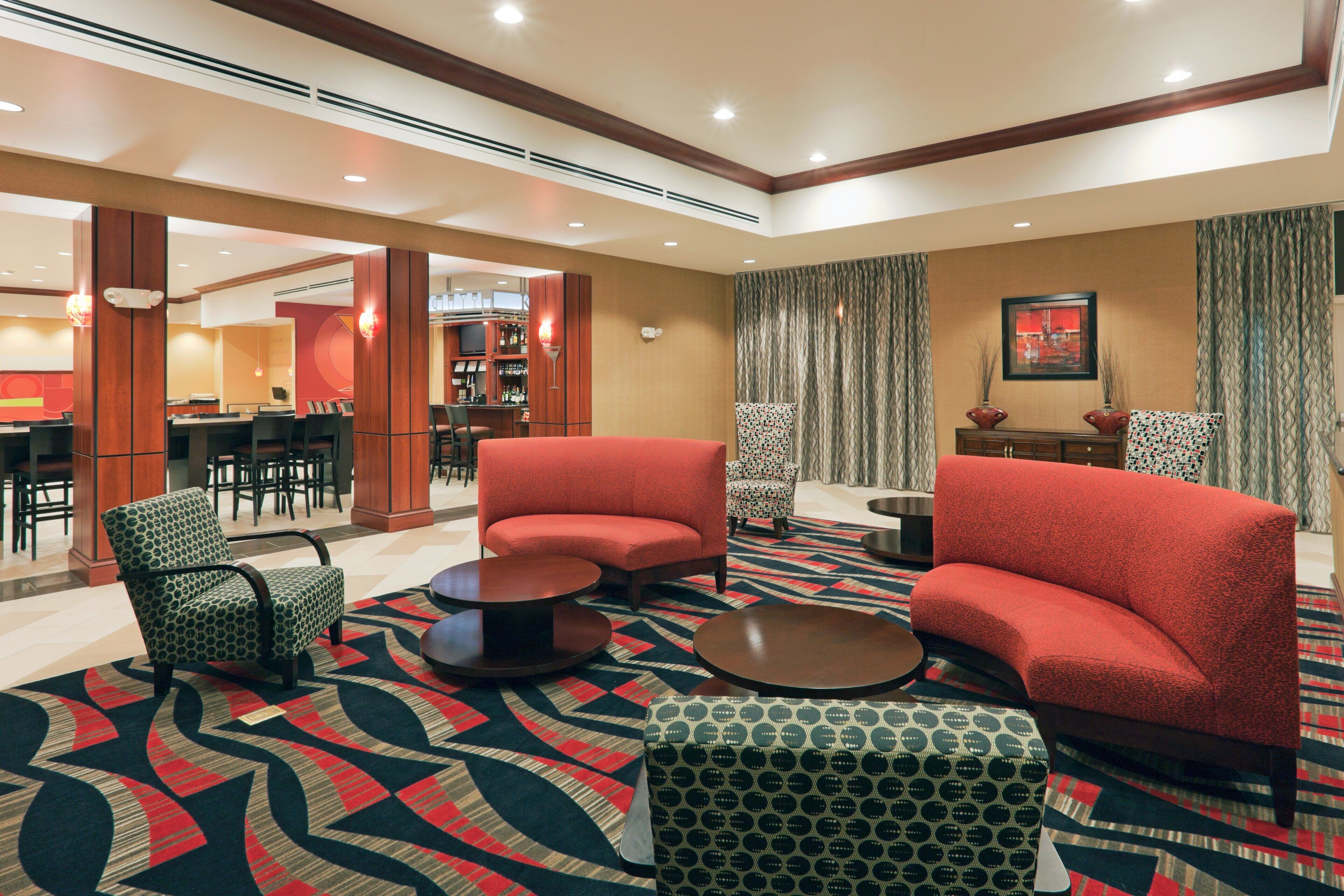 Un hall de hotel con sofás rojos, sillones estampados, una zona de bar y una sección de comedor.