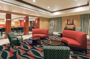 Un hall de hotel con sofás rojos, sillones estampados, una zona de bar y una sección de comedor.