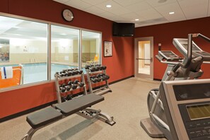 A gym with exercise equipment, a pool, and a clock on the wall.