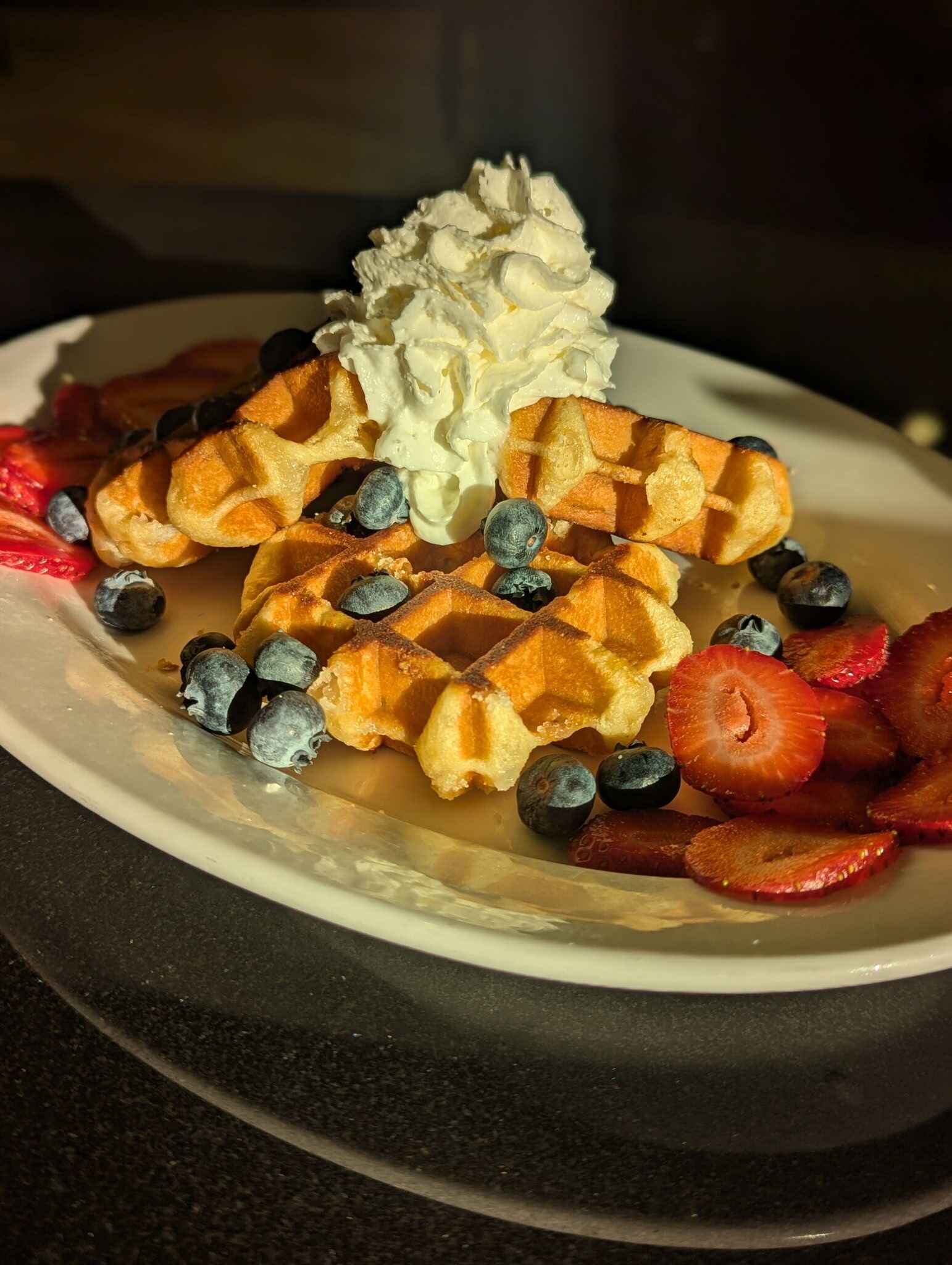 A plate of waffles with whipped cream, blueberries, and sliced strawberries.