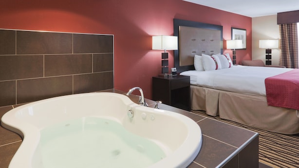 A hotel room with a large bathtub, a bed with a red blanket, and a nightstand with a lamp. - Holiday Inn Hotel & Suites Lima by IHG (Lima)