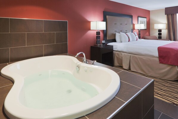 A hotel room with a large bathtub, a bed with a red blanket, and a nightstand with a lamp. - Holiday Inn Hotel & Suites Lima by IHG (Lima)