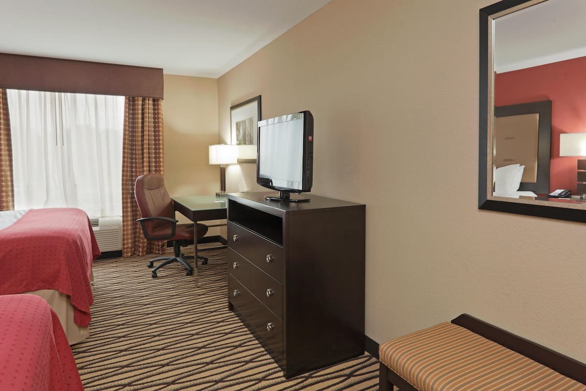 A hotel room with two beds, a desk with a computer, a chair, a lamp, and a mirror.