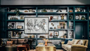 Una sala de estar acogedora con una pared verde oscuro, un cuadro abstracto grande y una variedad de fotos enmarcadas y objetos decorativos en estanterías.