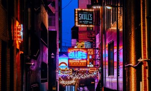 Kapea katu, jonka varrella on kirkkaasti valaistuja rakennuksia, ja näkyvillä on muun muassa kyltti, jossa lukee ”Skulls” ja ”Bourbon Street Blues”.