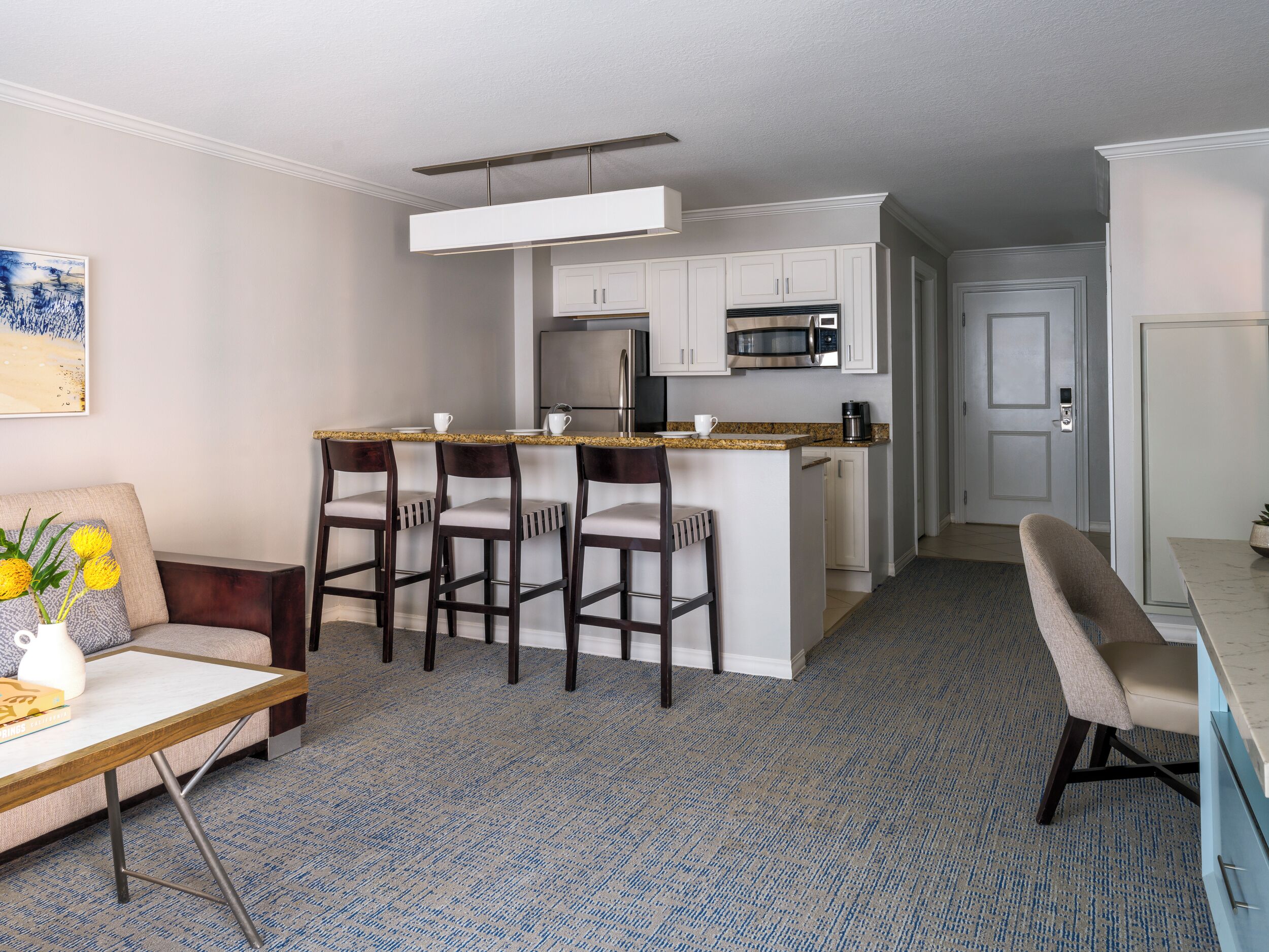 A compact living space with a kitchenette, a dining area with bar stools, and a seating area with a sofa and a side table.