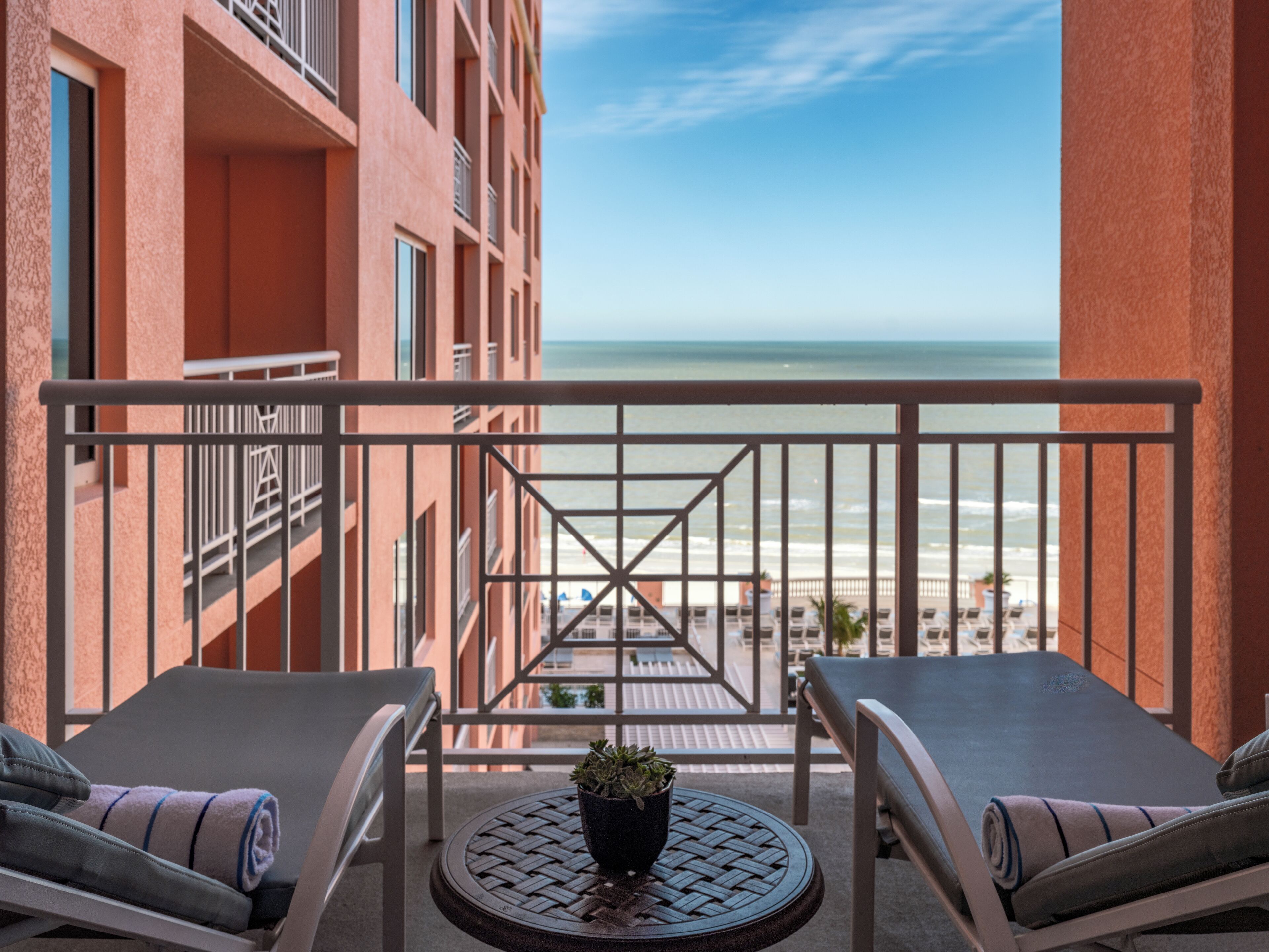 Un balcone con due poltrone, un tavolino e una pianta, con vista su una spiaggia e l'oceano.