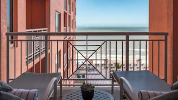 A balcony with two lounge chairs and a small table with a plant, overlooking a beach and ocean.
