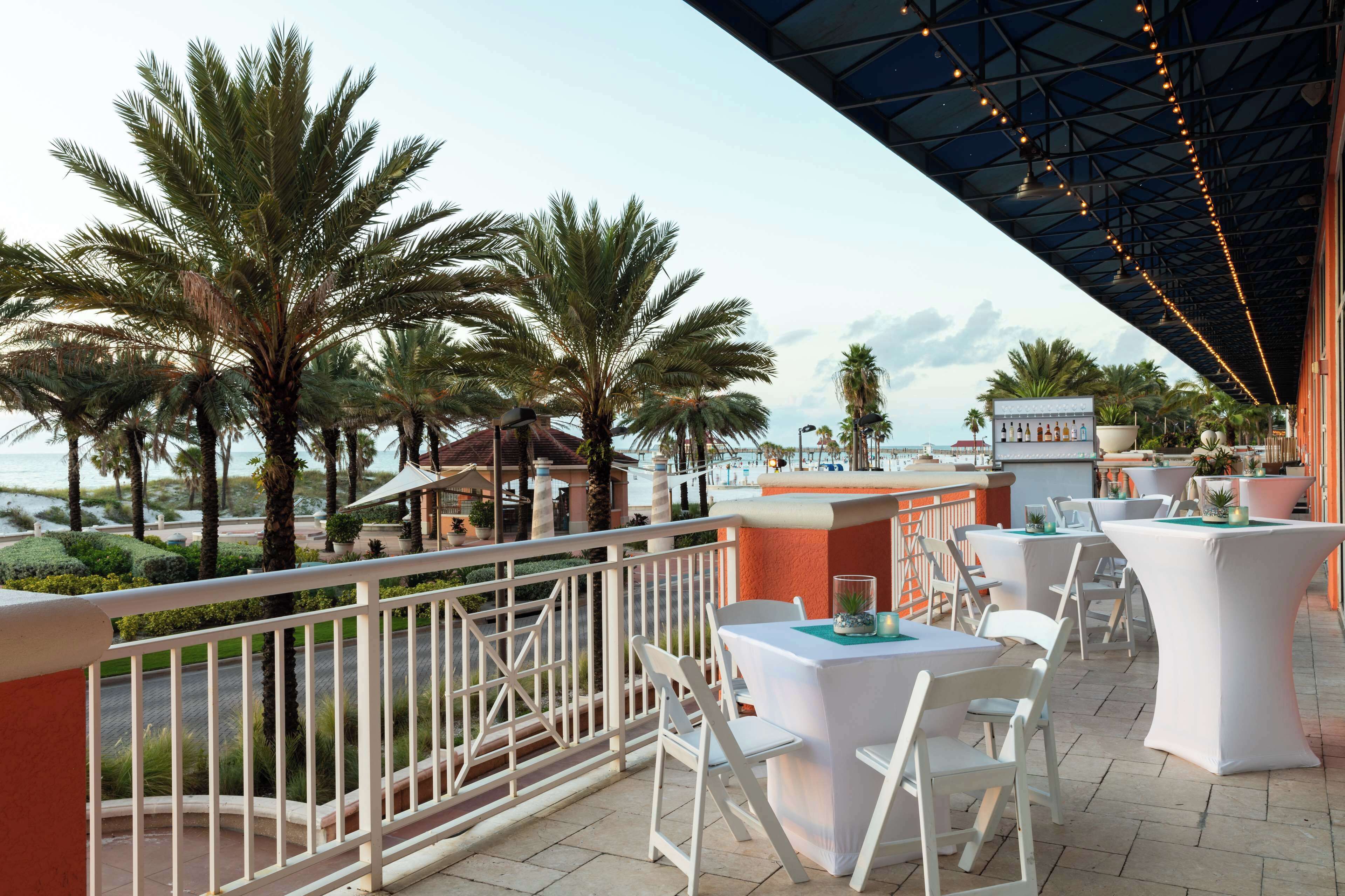 An outdoor dining area with white tables and chairs, overlooking a landscaped garden and the sea.