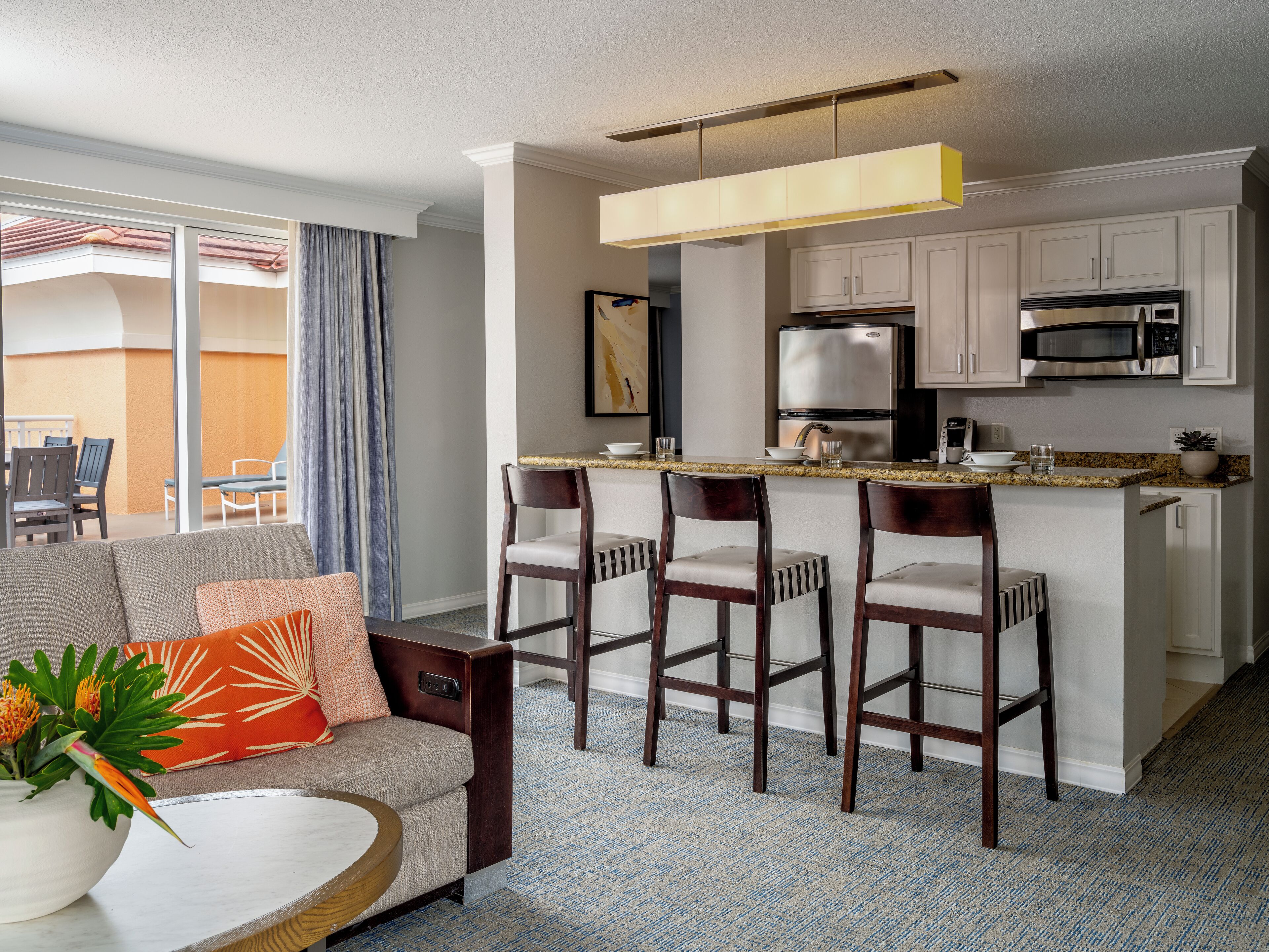 A modern hotel room with a living area, a kitchen, and a balcony.