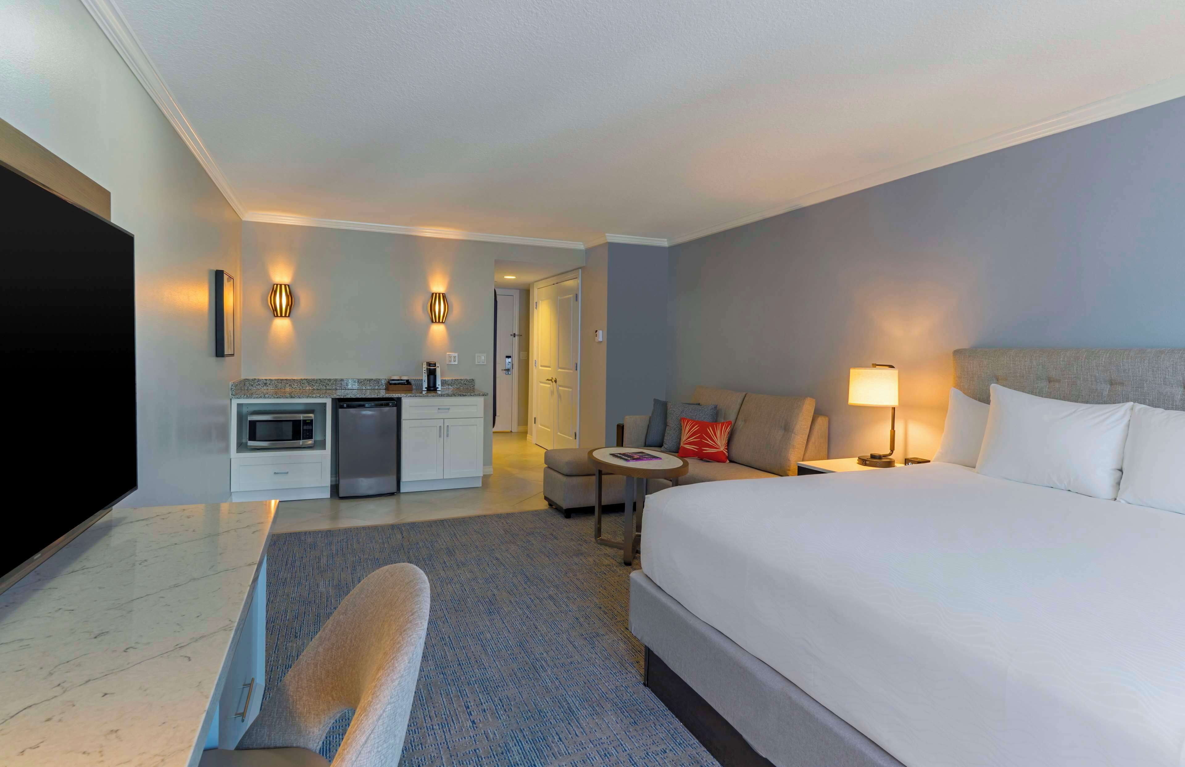 Une chambre d’hôtel dotée d’un grand lit, d’un téléviseur à écran plat, d’une kitchenette et d’un coin salon avec une table et des chaises.