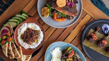 A table with various dishes including grilled fish, hummus, and a salad.