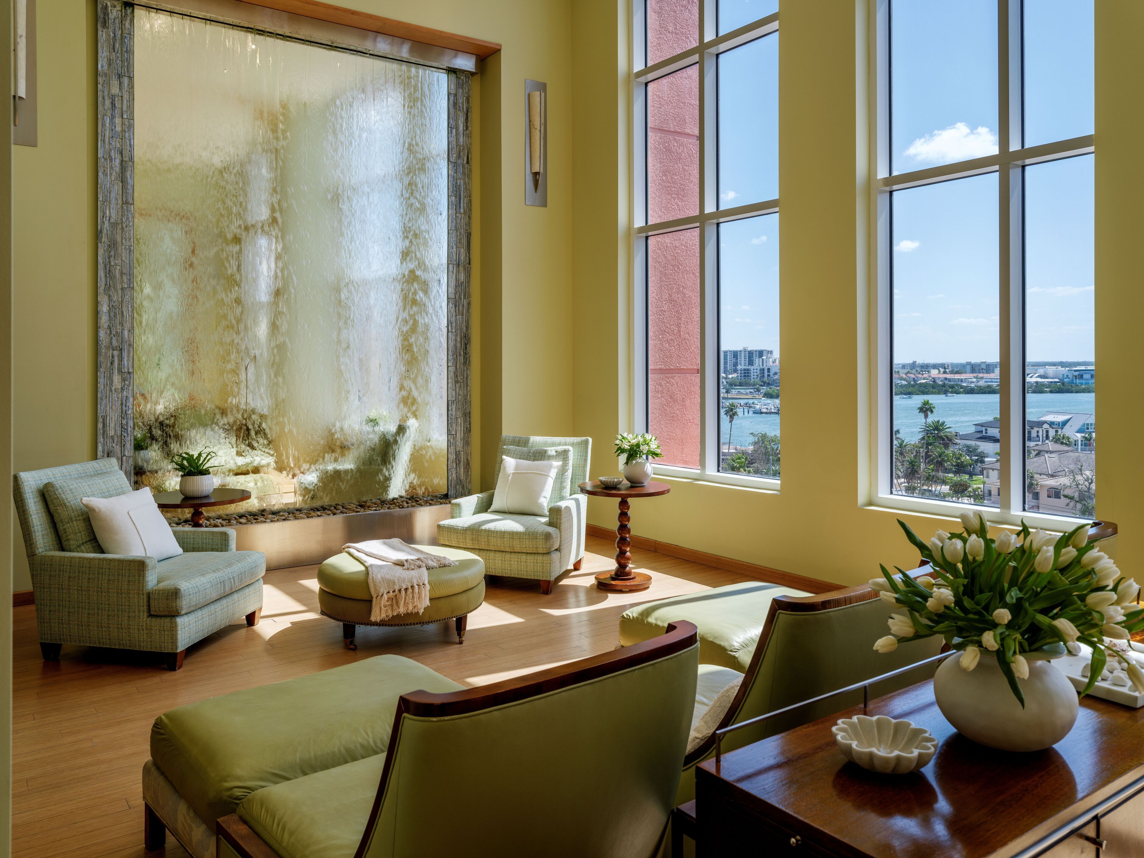A spacious living room with a large window offering a view of the city. There are comfortable seating areas and a decorative wall feature.