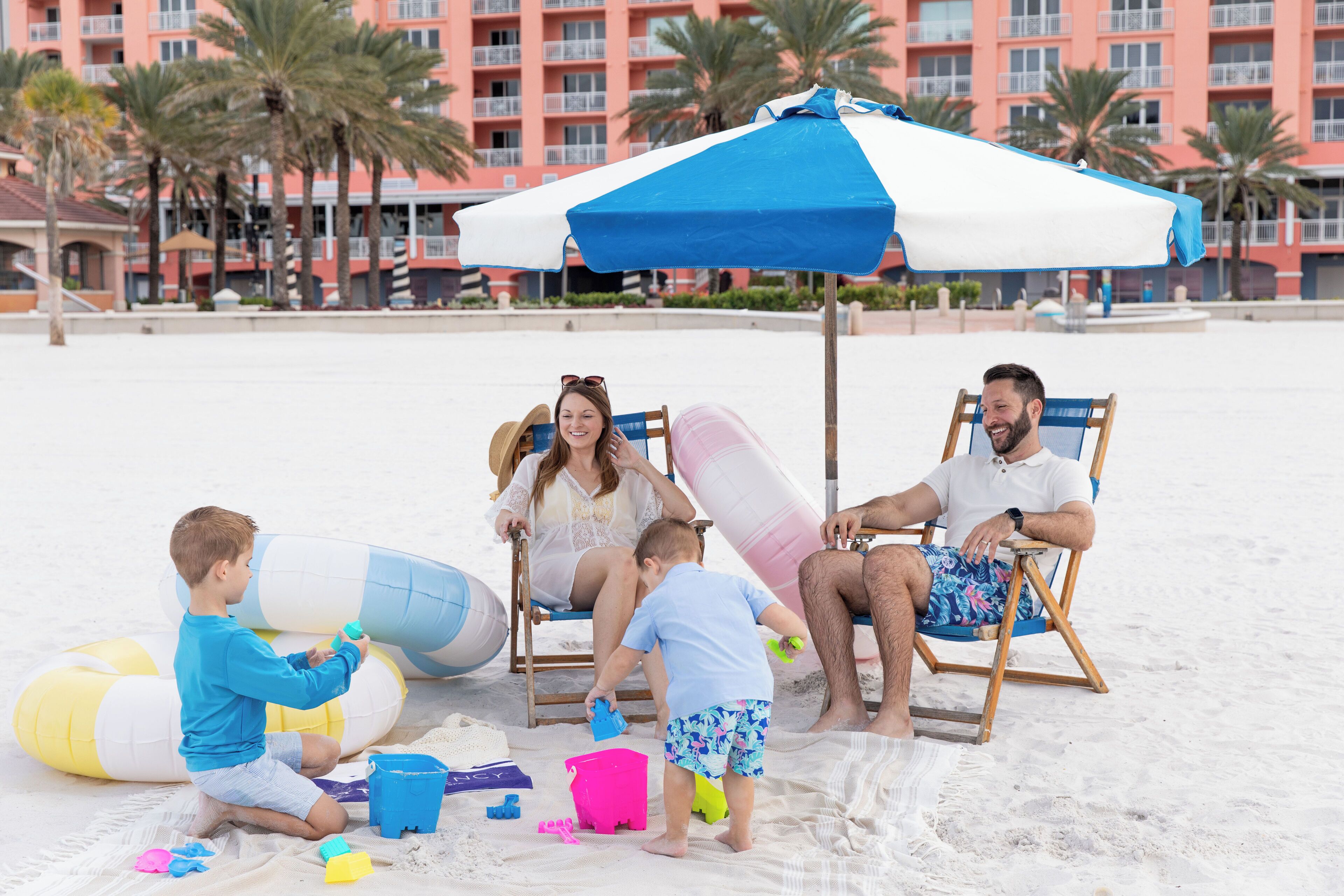 A beach scene with a family, including a child playing with toys, a woman in a chair, and a man in a beach chair.