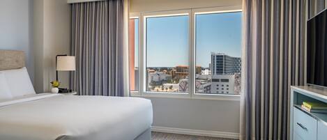 A hotel room with a large bed, a desk with a lamp, a TV, and a window with curtains.
