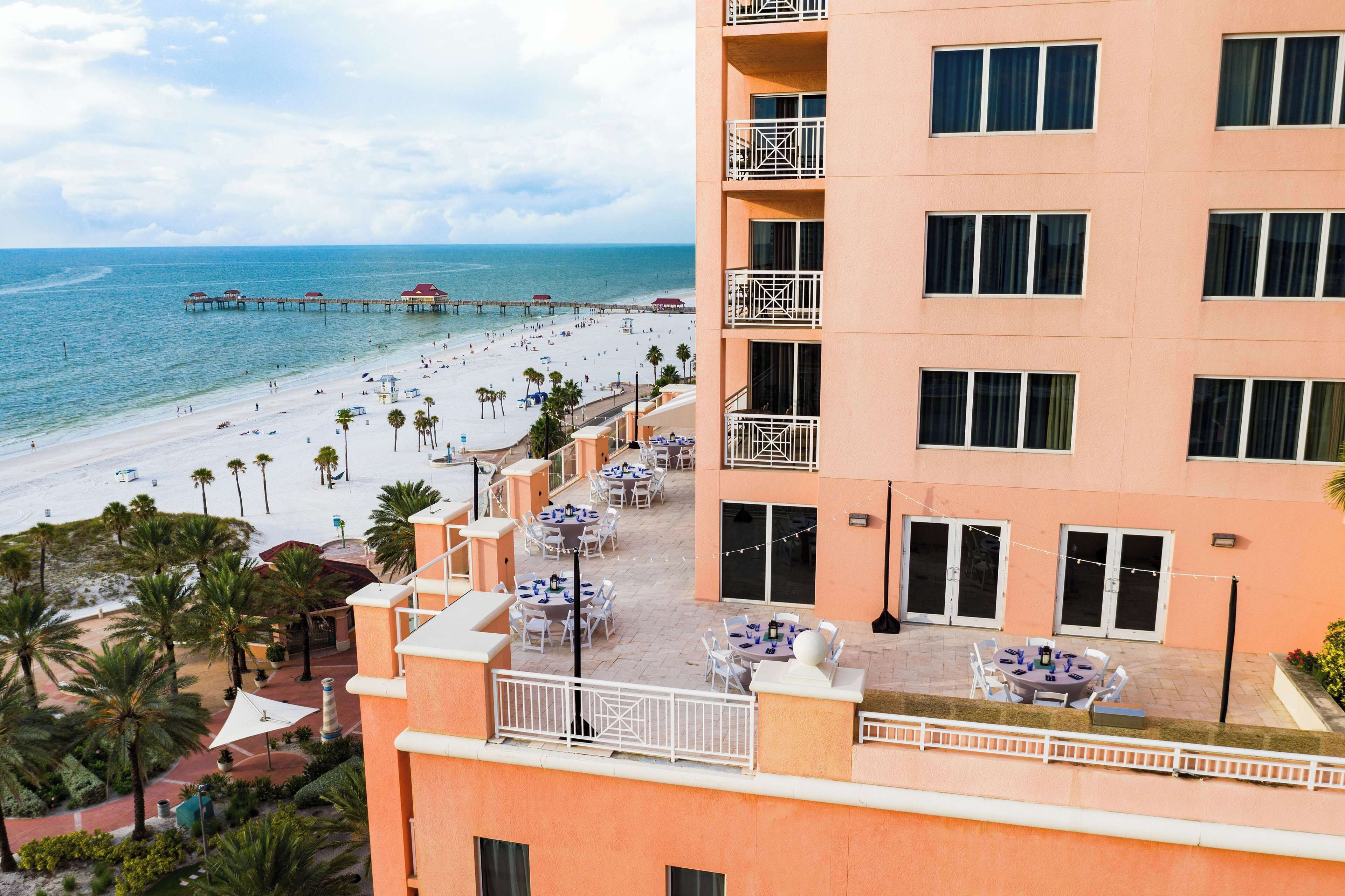 Un hotel con vista al mar, mobiliario exterior y un muelle al fondo.