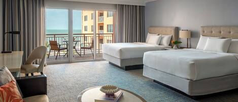Habitación de hotel con dos camas, un sofá, una mesita y un balcón con vista al mar.