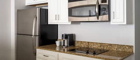 Una cocina con gabinetes blancos, electrodomésticos de acero inoxidable, encimera de granito y microondas integrado.