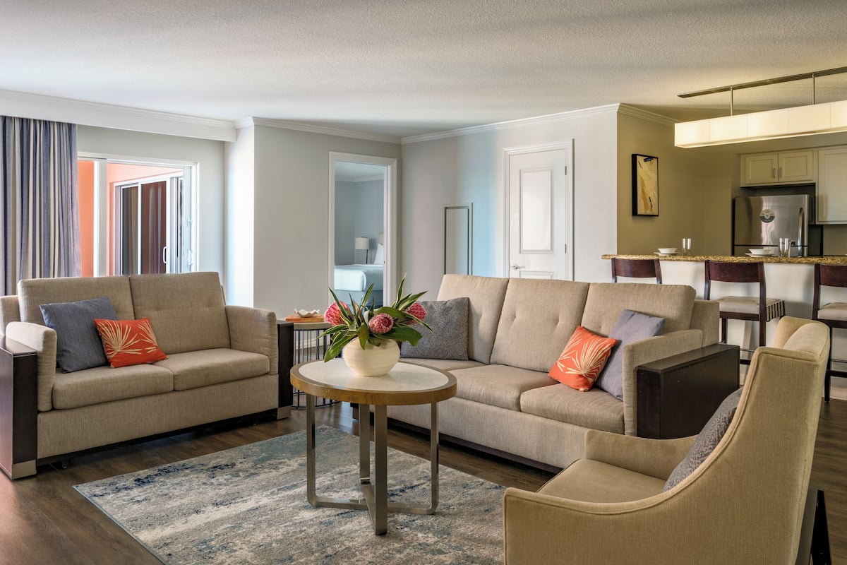 A modern living room with two sofas, a round coffee table, and a chair. There is a kitchen area visible in the background.