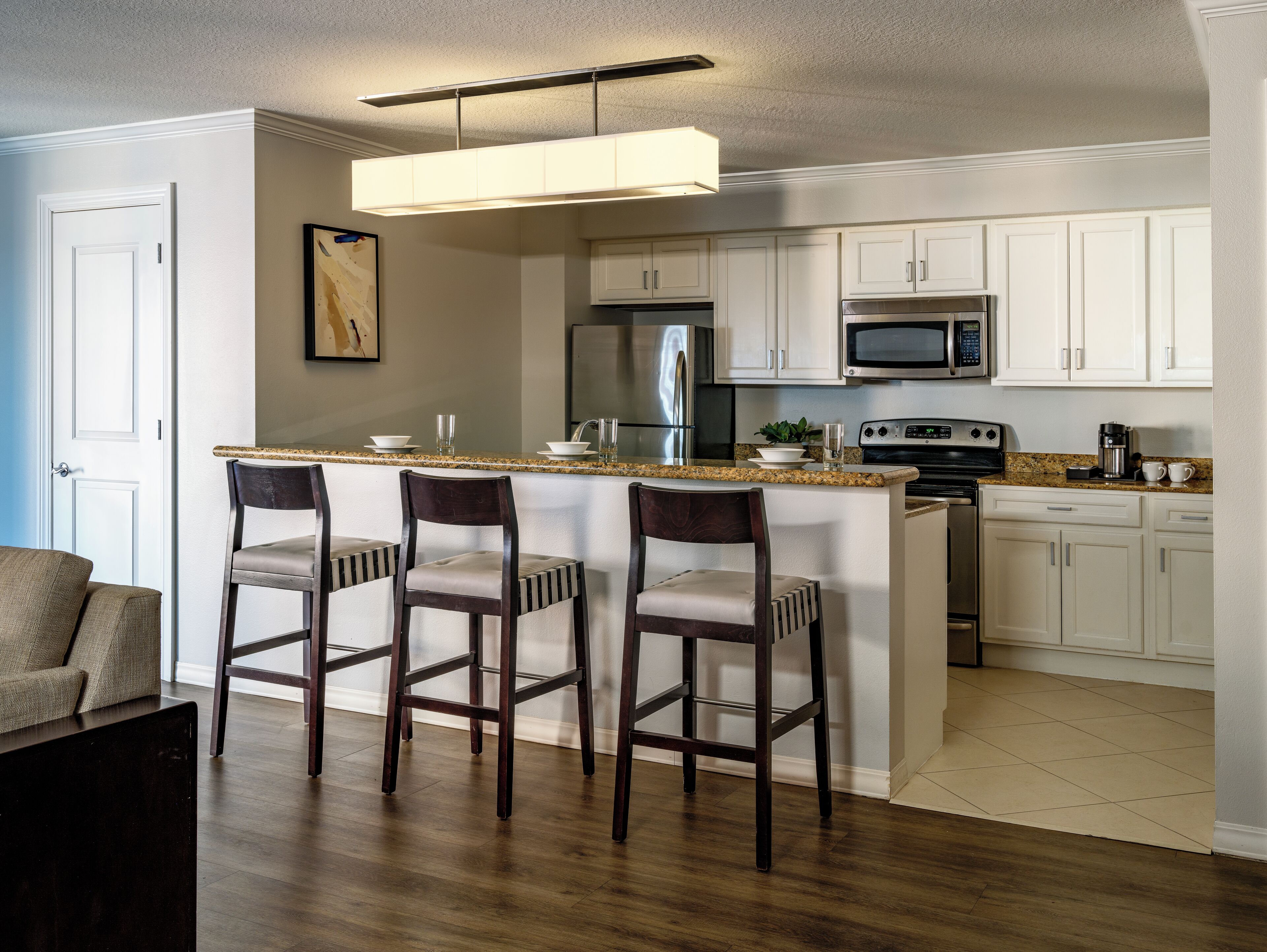A kitchen with a central island, bar stools, a refrigerator, microwave, oven, and a pendant light.
